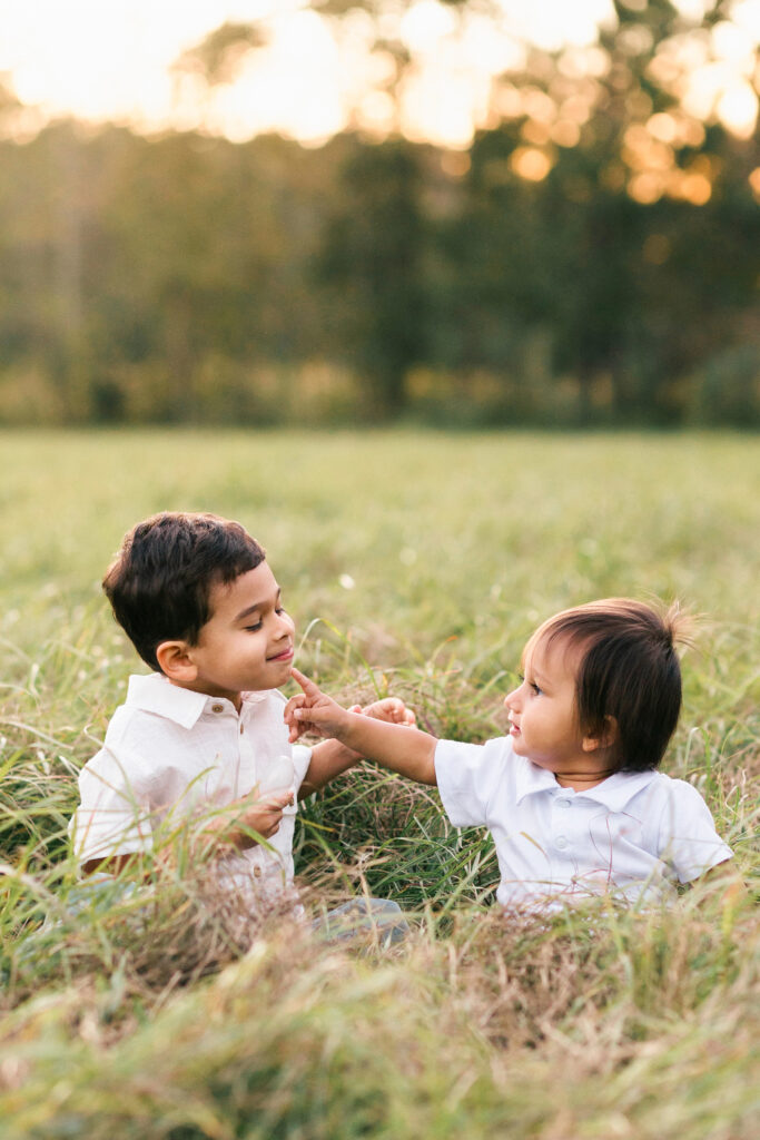 two little boys sitting in a jacksonville field looking at each other and smiling