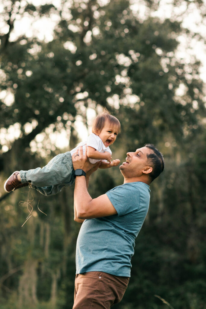 a father swings his one year old up in the air while they both laugh